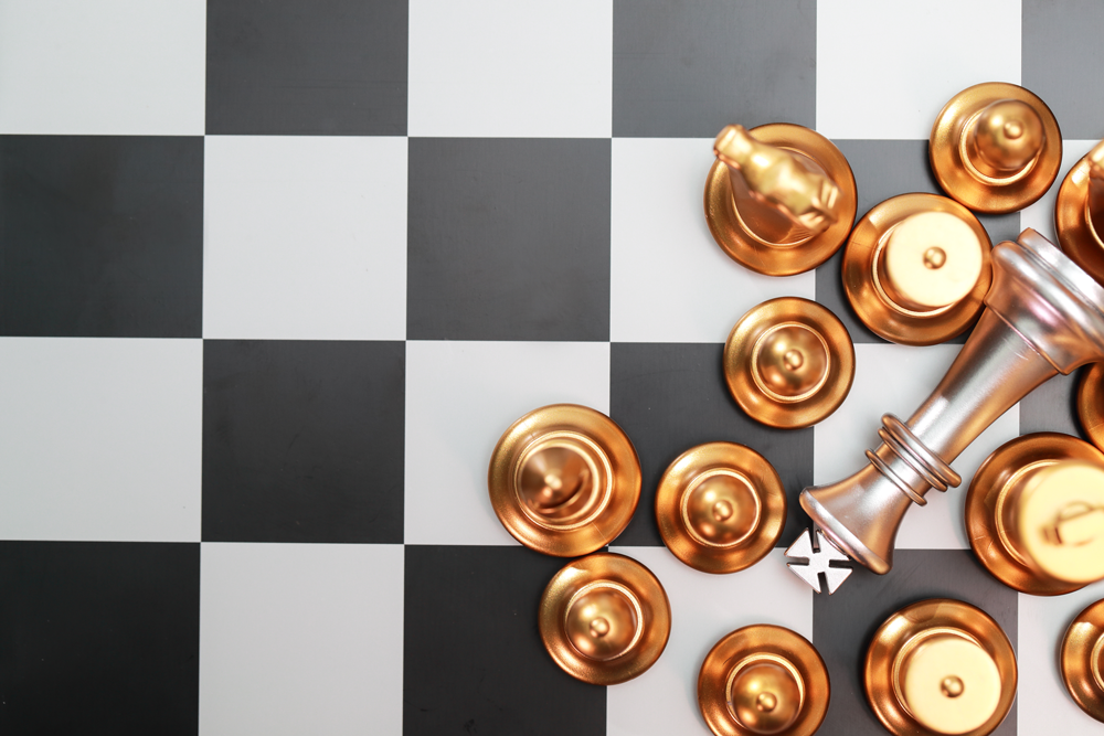 Chess board with the king laying down and other chess pieces surrounding it