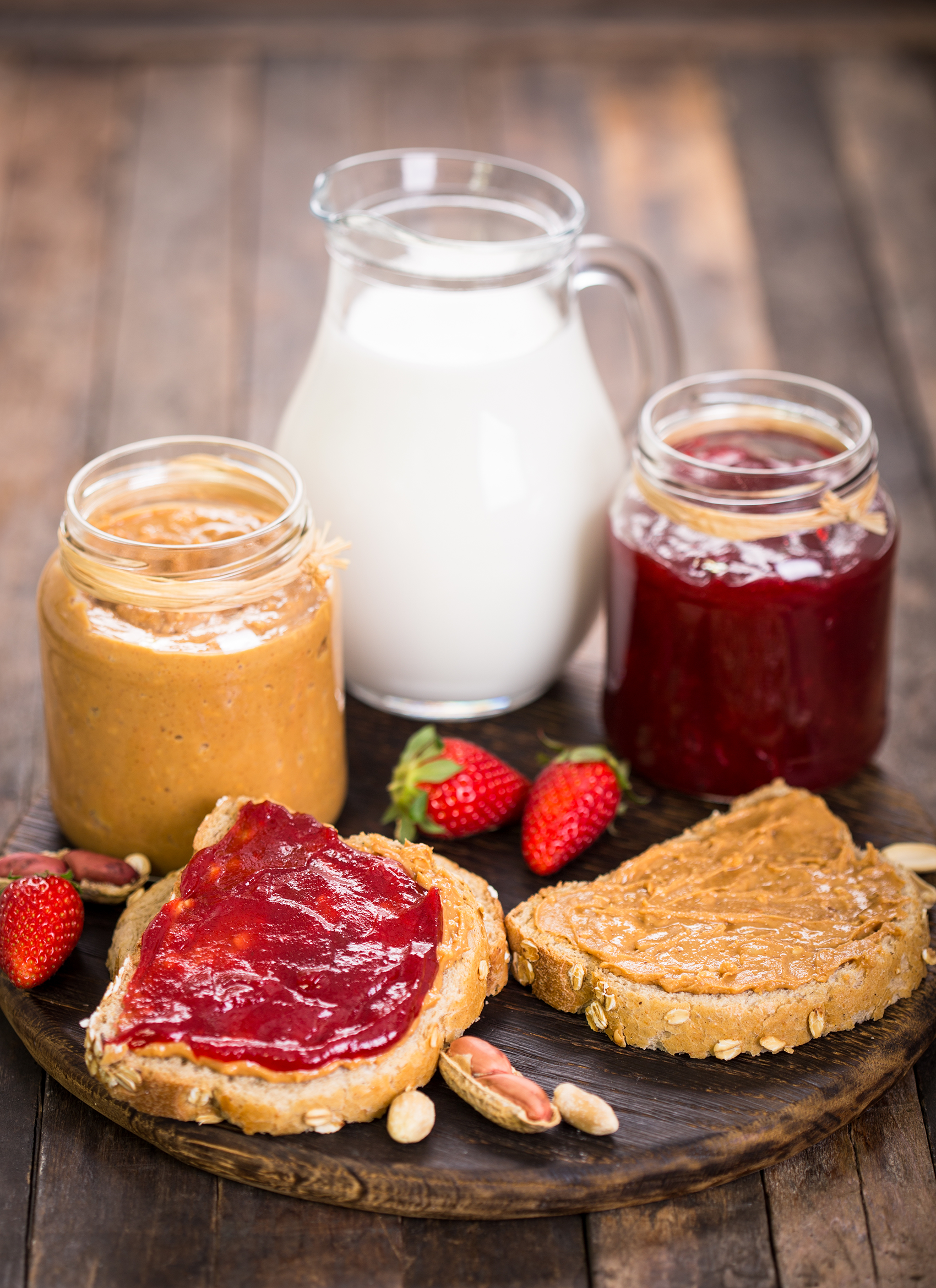 Peanut butter and jelly sandwich with a jar of peanut butter, a jar of jelly, and a pitcher of milk.